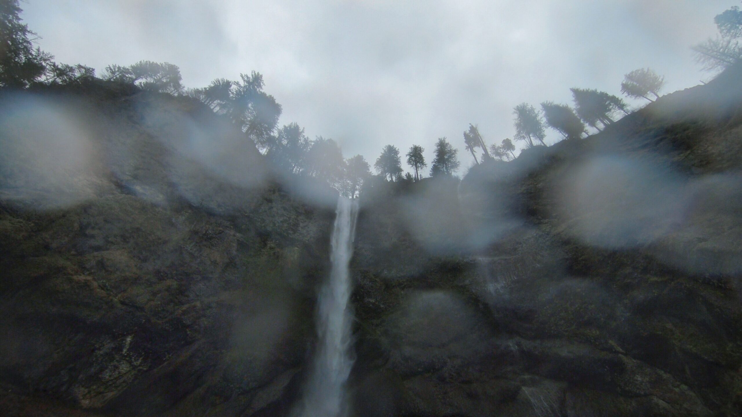 Rainy view looking up at the Multnomah Falls coming over the cliffs edge