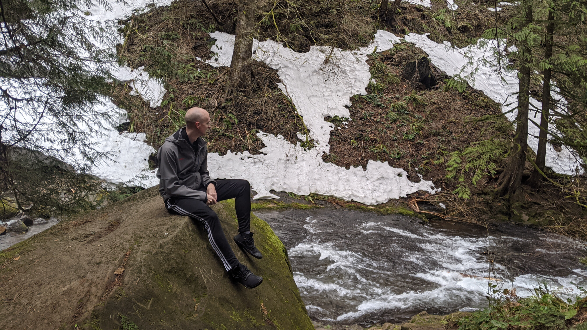 Traveler sitting on a rock in front of a flowing river in the forest